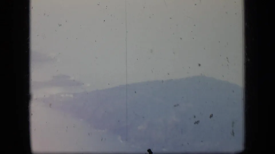 1970 Puerto Rico aerial frame with a distant hazy mountain silhouette visible through the airplane window and aged film texture.