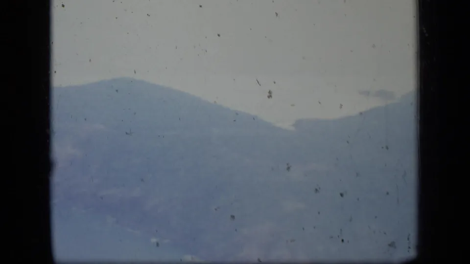 1970 Puerto Rico home-movie frame showing hazy blue-green mountains from an airplane window, with visible film dust and frame edges.