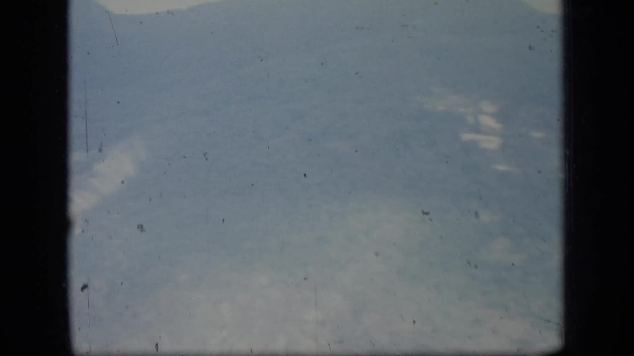 1970 Puerto Rico home-movie frame showing a distant hazy mountain ridge with dark film-gate borders and visible dust specks.