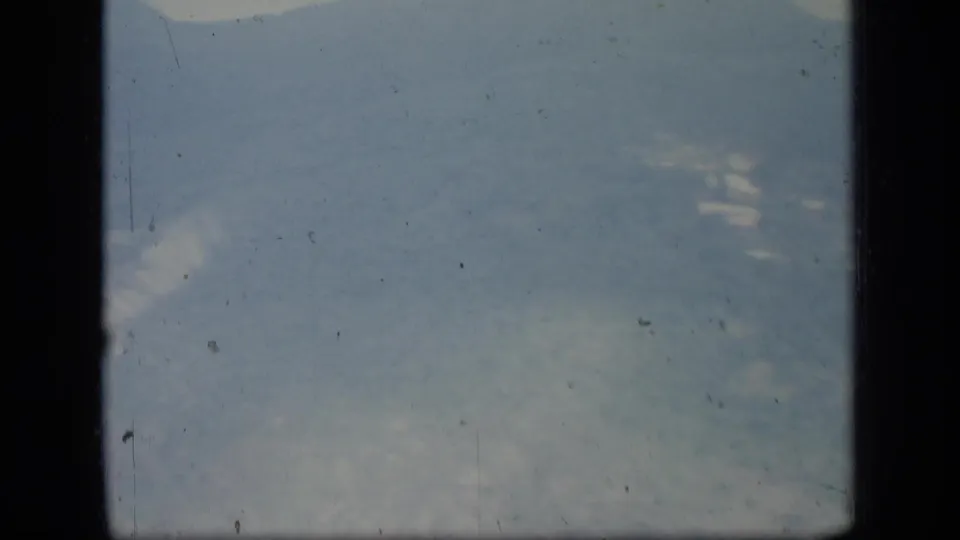1970 Puerto Rico home-movie frame showing a distant hazy mountain ridge with dark film-gate borders and visible dust specks.