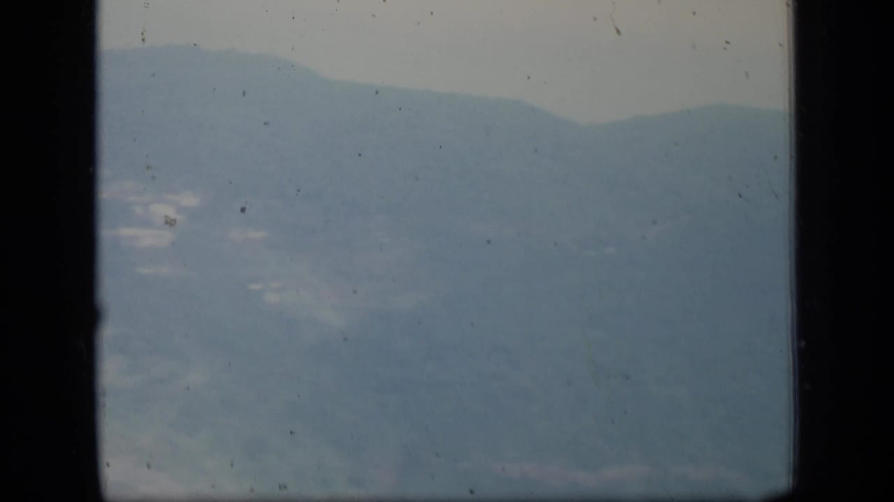 1970 Puerto Rico landscape frame with layered mountain slopes, pale haze, black frame edges, and scattered film dust.