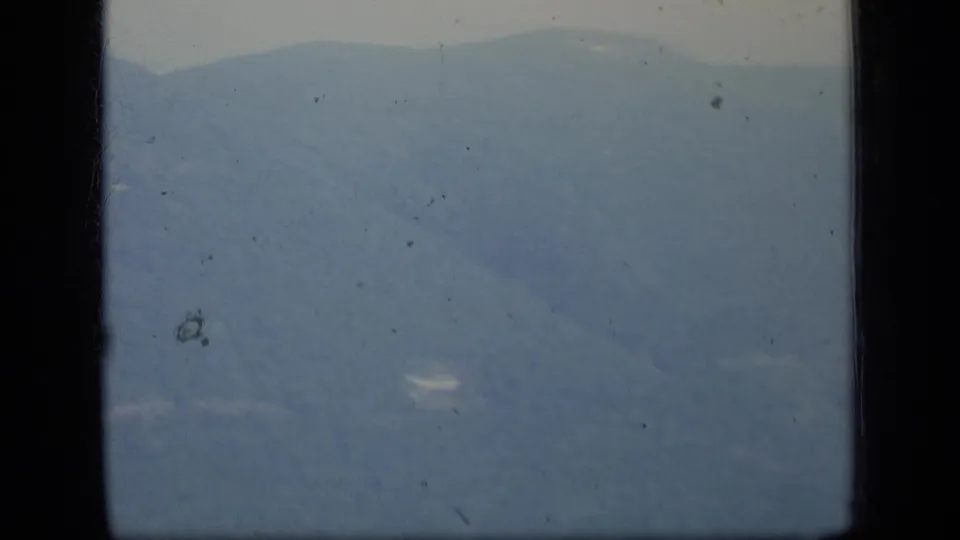 1970 Puerto Rico 8mm still showing a soft mountain valley, ridge line, pale haze, and visible film speckling.