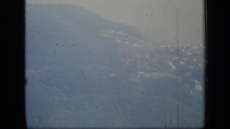 1970 Puerto Rico aerial view through an airplane window, with hazy blue mountains and small light buildings on the slopes.