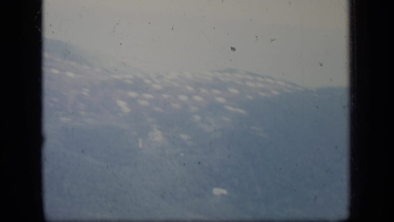 Hazy 1970 Puerto Rico hillside settlement and mountain ridge viewed from inside an airplane, partly blocked by dark window framing.