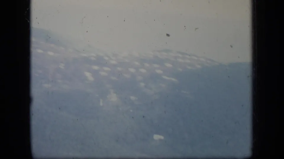 Hazy 1970 Puerto Rico hillside settlement and mountain ridge viewed from inside an airplane, partly blocked by dark window framing.