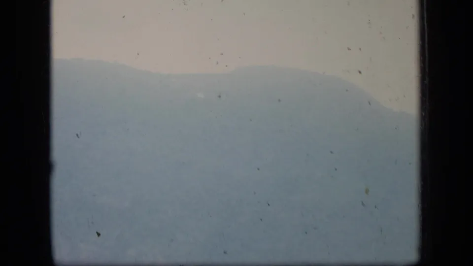 Hazy 1970 Puerto Rico aerial view with a distant mountain silhouette and dark airplane window framing on both sides.