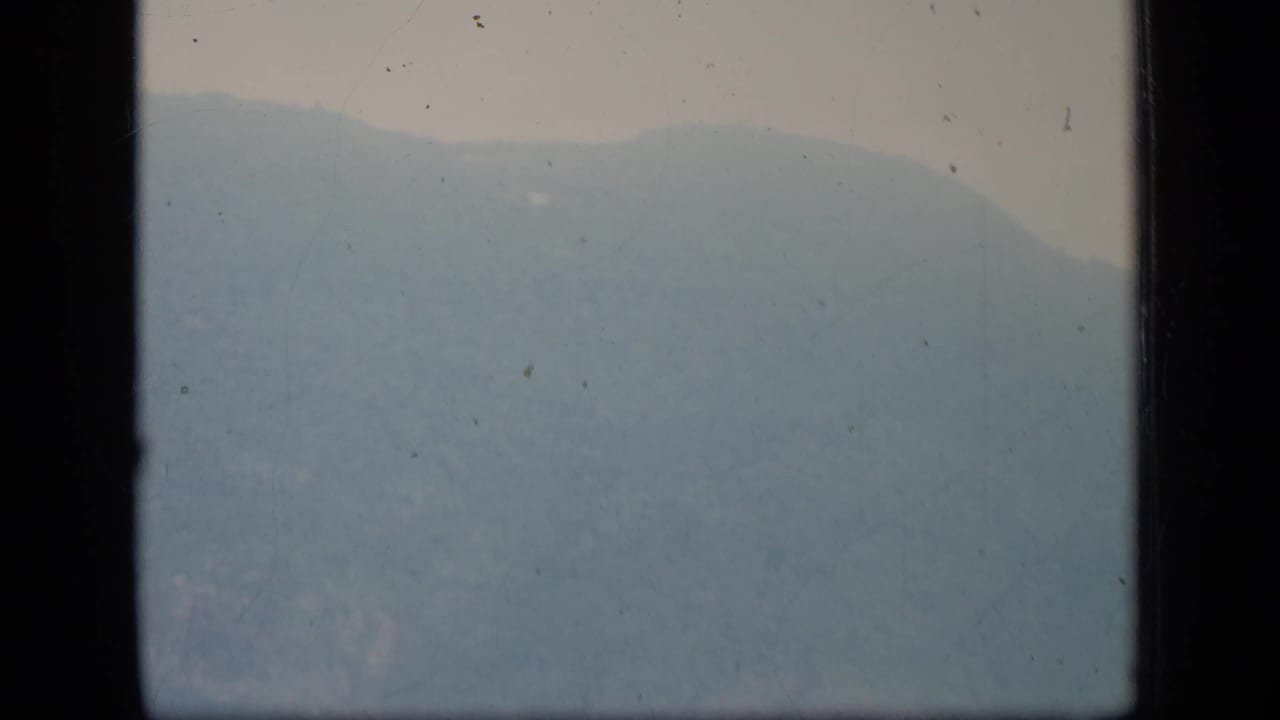 Hazy Puerto Rico hillside on 1970 8mm film, with soft exposure, pale sky, and dark gate edges.