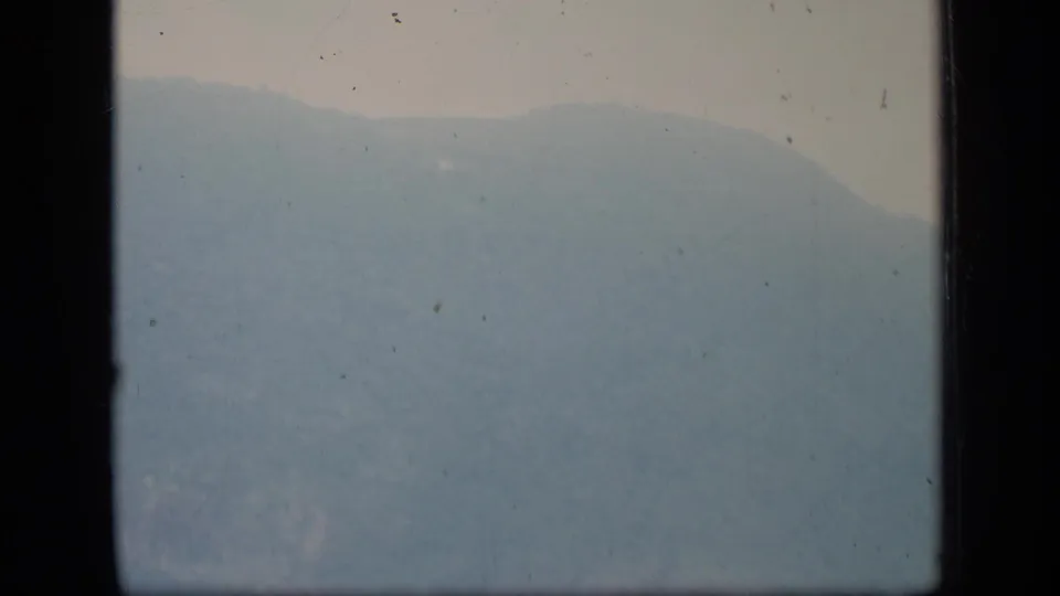 Hazy Puerto Rico hillside on 1970 8mm film, with soft exposure, pale sky, and dark gate edges.