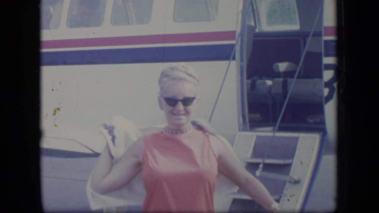 In 1970 Puerto Rico footage, a woman in a pink sleeveless dress smiles while stepping down from a small aircraft.