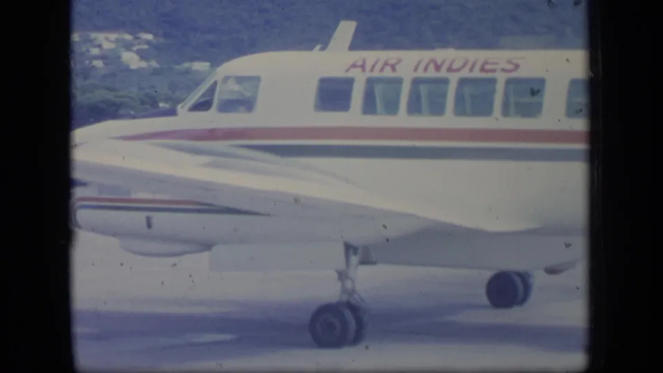 Side detail of the Air Indies aircraft shows passenger windows, landing gear, and fuselage striping on the tarmac.