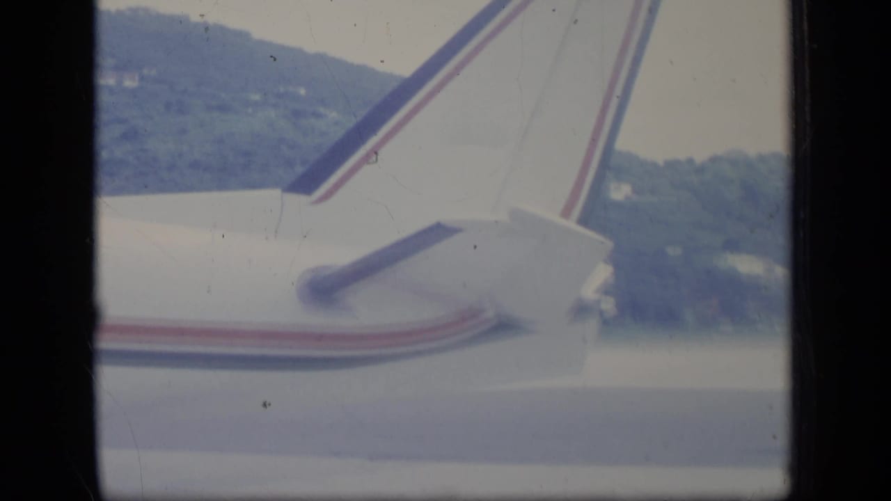 Airplane tail seen through a window with green hills beyond.
