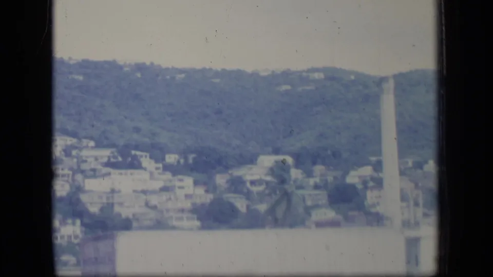 Aerial Puerto Rico frame showing hillside buildings and a tall industrial smokestack in a hazy 8mm view.