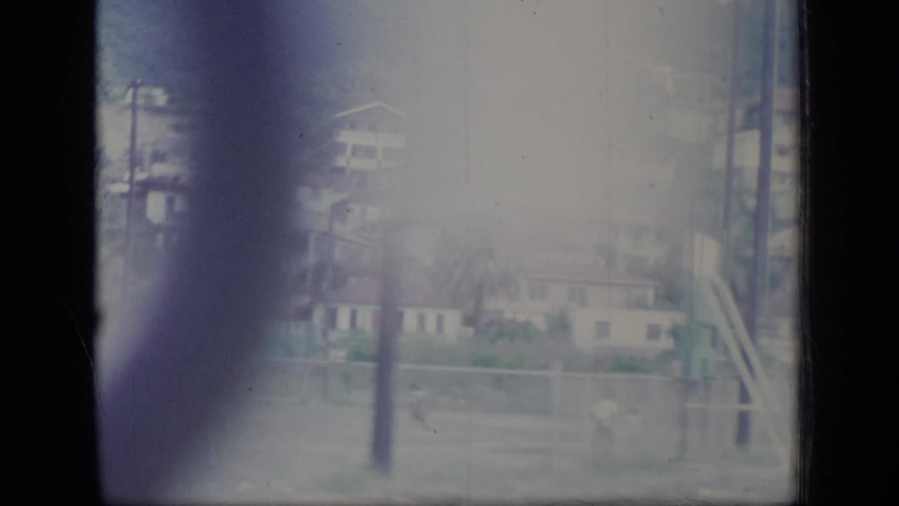 Soft 8mm frame of hillside houses behind utility poles and pale flare.