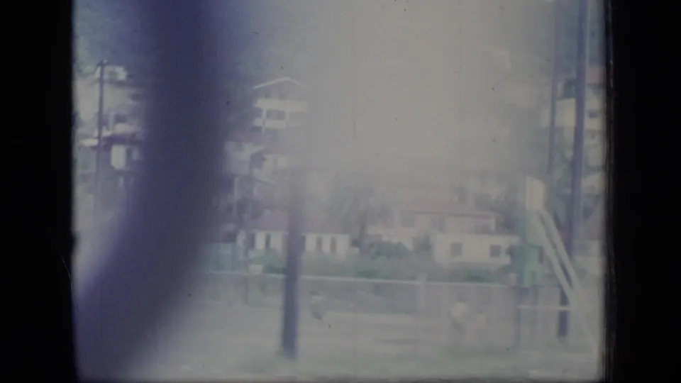 Puerto Rico 1970 home-movie frame with hillside homes, utility poles, foliage, and heavy purple flare at the film edge.