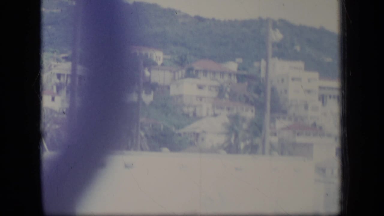 Hillside neighborhood with pale buildings, red roofs, foliage, and film-edge shadow.