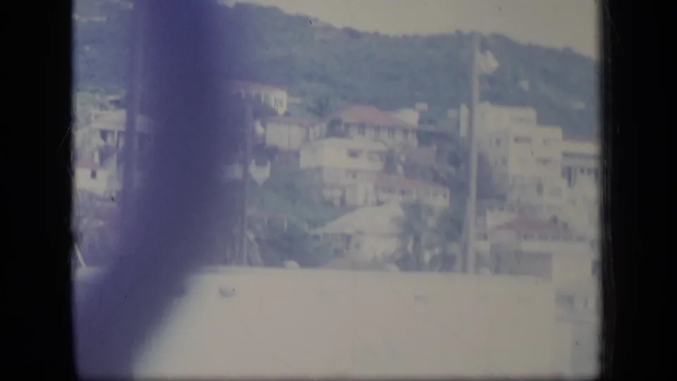 Puerto Rico 1970 8mm view of a hillside residential area with red-roofed homes, trees, and dark gate shadows at the sides.
