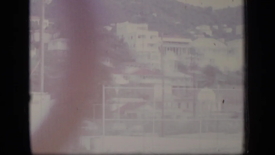 Puerto Rico 1970 home-movie still showing hillside homes, vegetation, wires, and a pale utility structure through faded exposure.