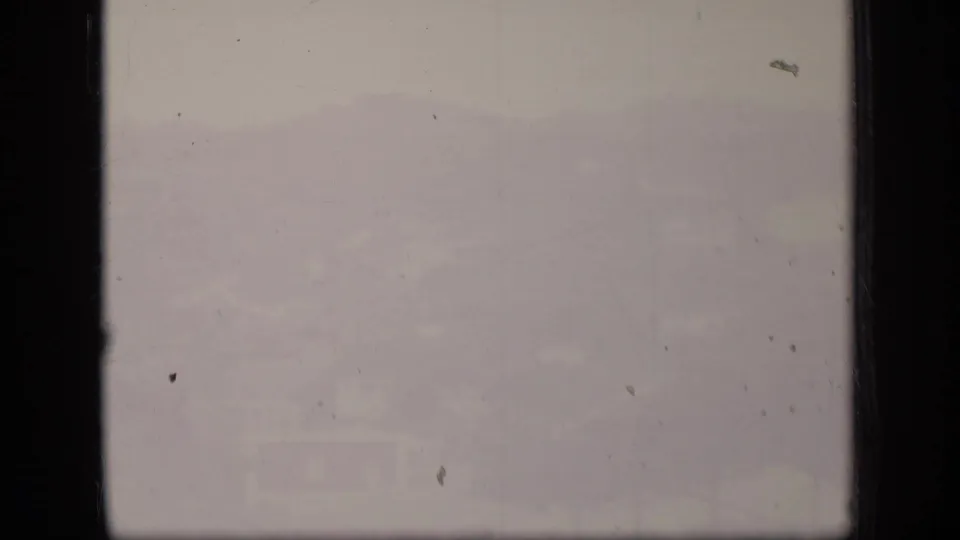 Overexposed Puerto Rico 1970 8mm frame with faint hillside forms, dust marks, scratches, and washed color across the film surface.