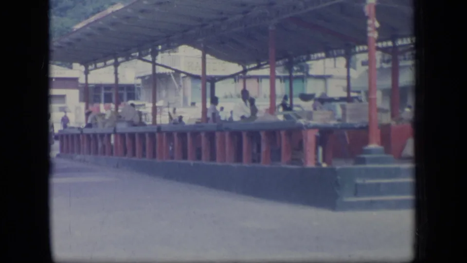 Soft 8mm frame of a Puerto Rico market area, with red railing, counters, people, and a covered roof structure.