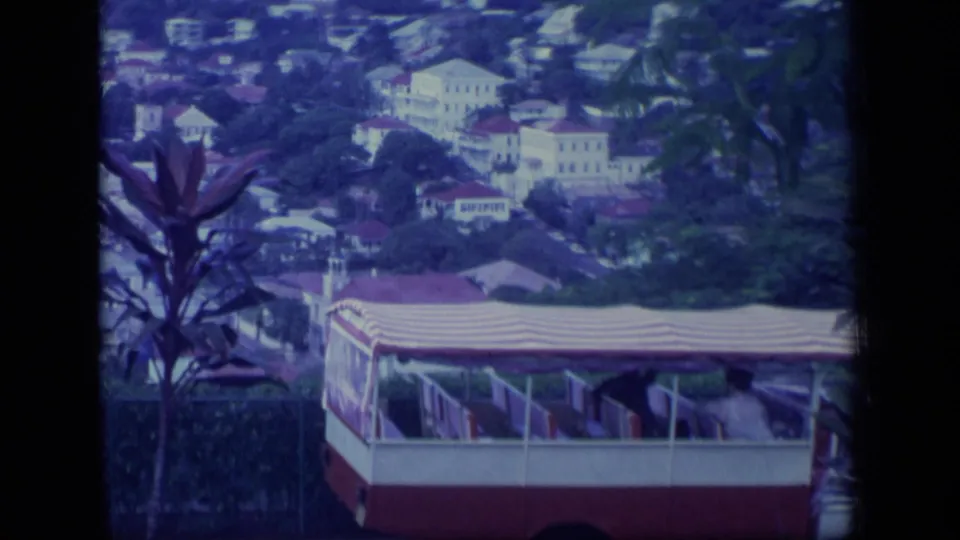 1970 Puerto Rico hillside view with white buildings, palm foliage, and a red-and-white cable-car or tram-like cabin in the foreground.