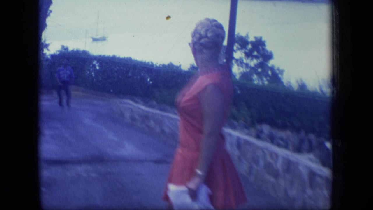Woman in a red dress turns away on a path with a blimp visible in the sky.