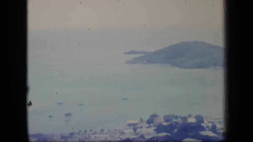 Wide 8mm Puerto Rico aerial view showing pale bay water, scattered boats, shoreline buildings, and a wooded mountain or island.