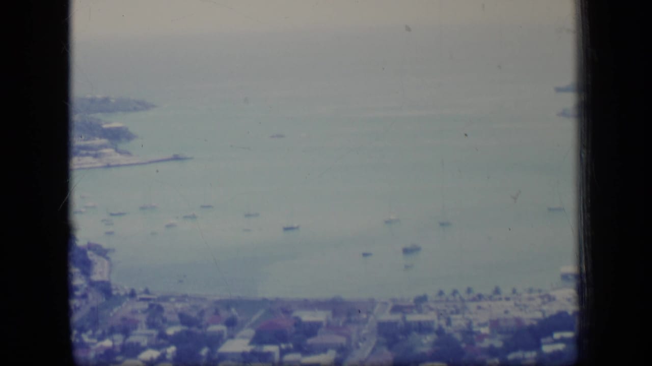 High 1970 Puerto Rico view of a bay, anchored boats, shoreline roads, and residential buildings divided by dark window framing.