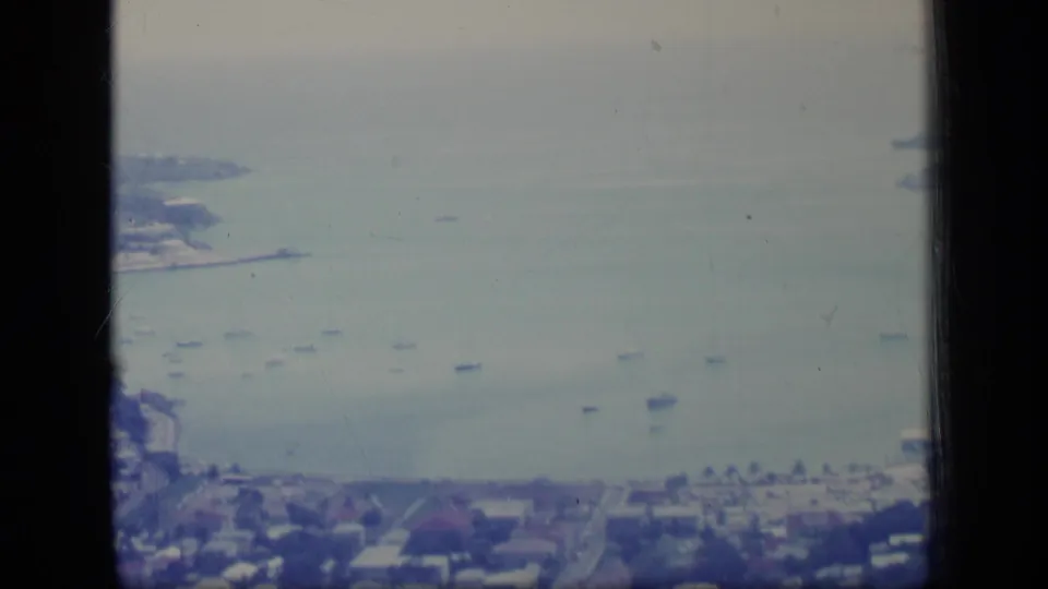 High 1970 Puerto Rico view of a bay, anchored boats, shoreline roads, and residential buildings divided by dark window framing.