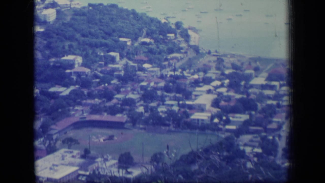 Elevated view of a waterfront suburb with houses, roads, boats, and a baseball field.