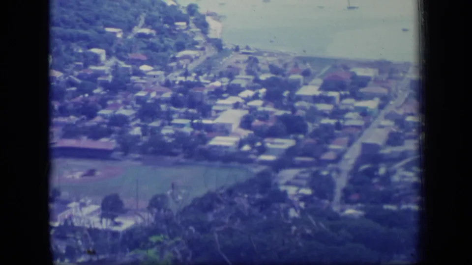 1970 Puerto Rico home-movie frame looking down on houses, roads, a bay shoreline, trees, and a baseball field near the lower edge.