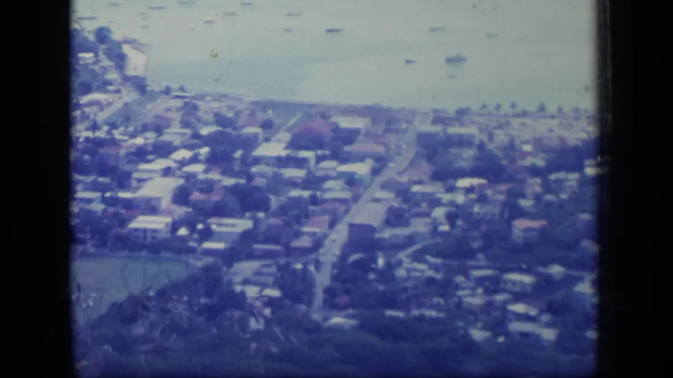 1970 Puerto Rico aerial frame showing a coastal suburb, anchored boats, shoreline roadways, low-rise homes, and soft blue 8mm color.