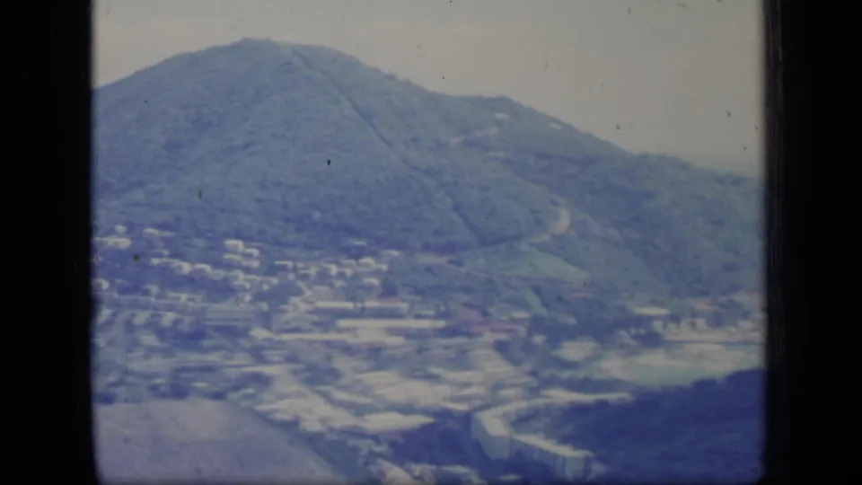 Puerto Rico 8mm aerial frame from 1970 showing a broad green mountain above roads, buildings, and open ground.