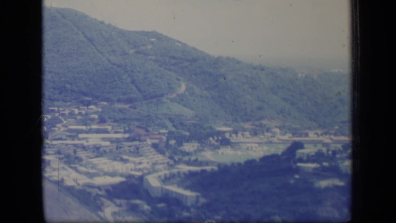 Green hills and valley settlement with roads, fields, and distant haze.