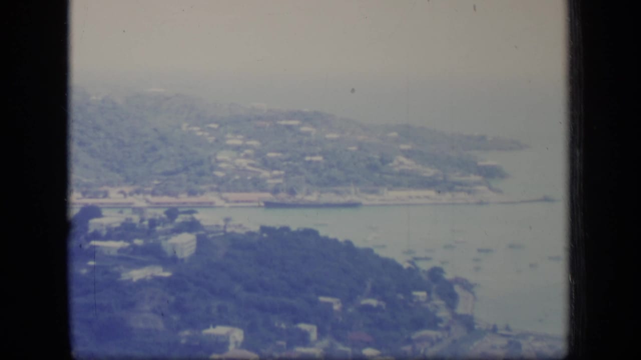 Coastal hillside and harbor with small boats visible in hazy blue-green film color.