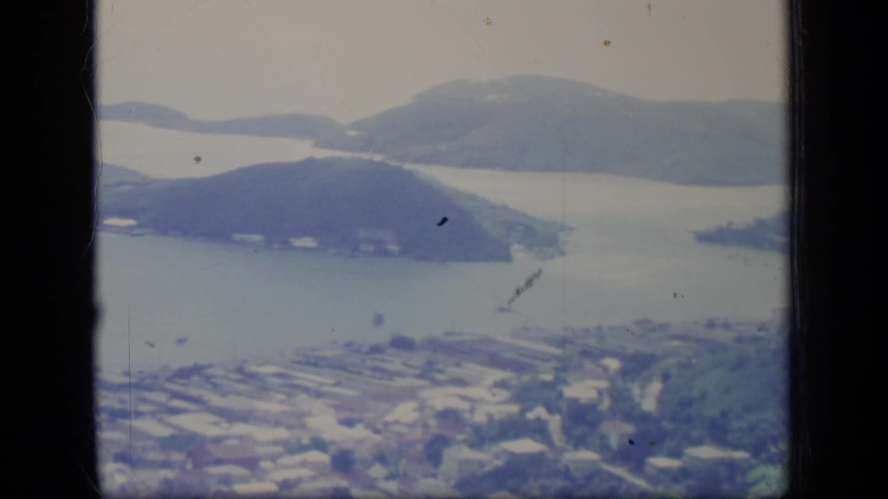 Soft 8mm view over a bay with hills, water, buildings, and dark film borders.