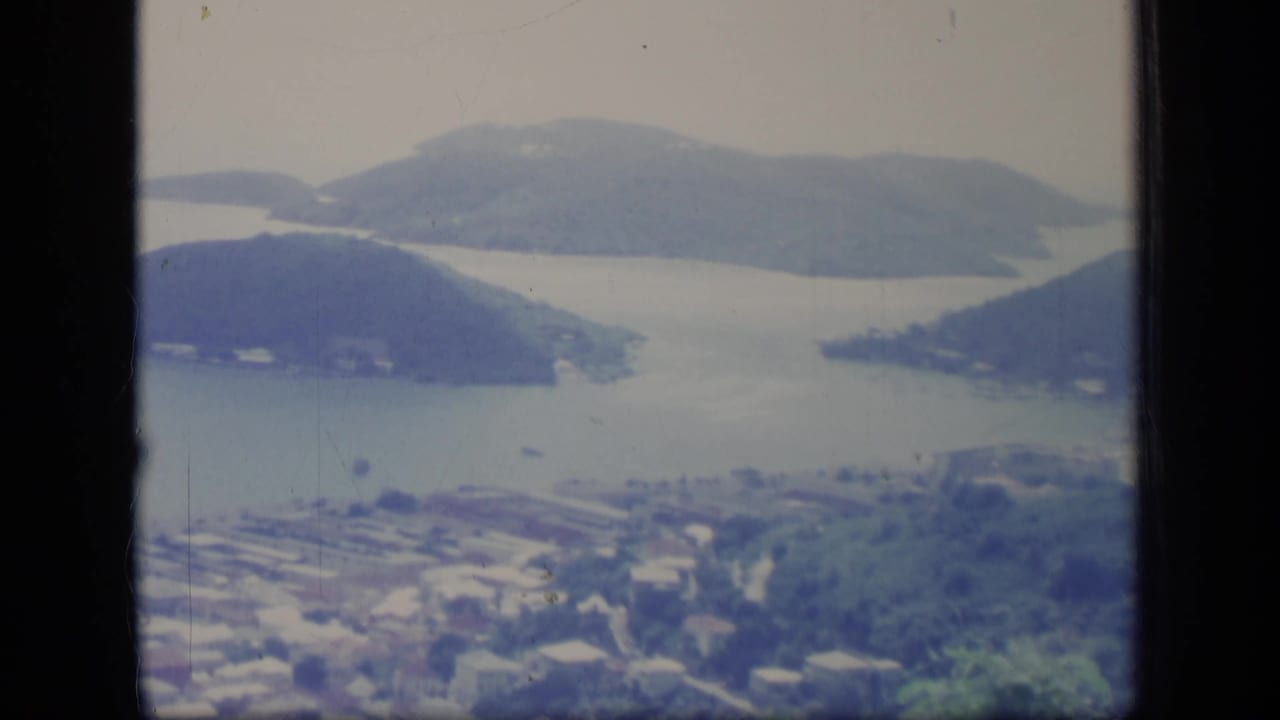 Faded 1970 Puerto Rico 8mm view of a bay, wooded headlands, small boats, and a coastal settlement from a high vantage point.