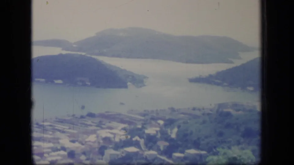 Faded 1970 Puerto Rico 8mm view of a bay, wooded headlands, small boats, and a coastal settlement from a high vantage point.