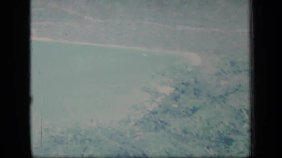 Aerial or elevated 1970 Puerto Rico view of turquoise coastal water, shore, and green land through faded 8mm color.
