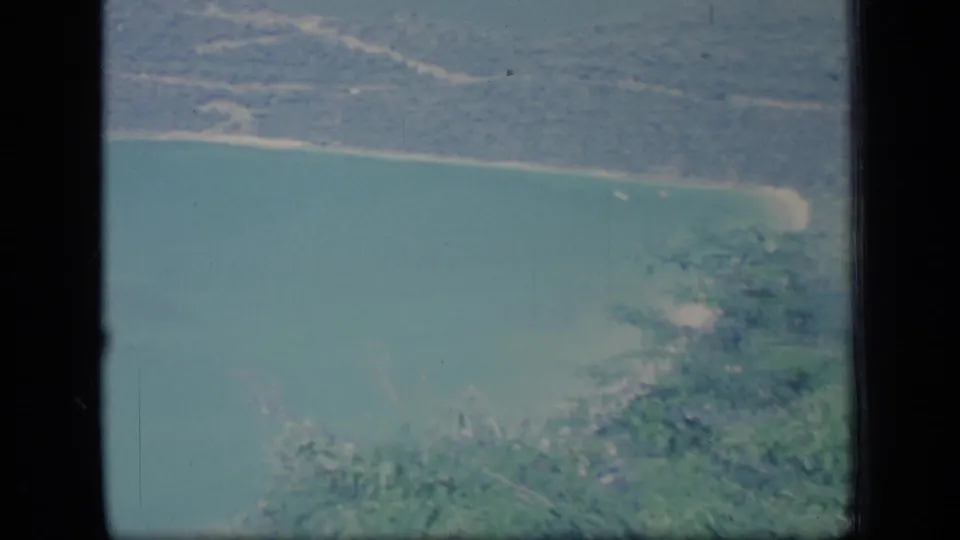 Elevated Puerto Rico coastal view showing turquoise water, wooded shoreline, hills, and small settlement areas on 8mm film.