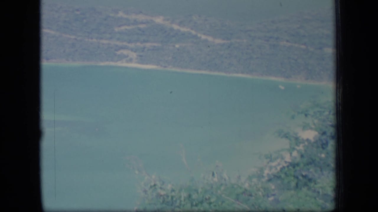 Aerial view of turquoise water, sandy shore, and forested coastline seen through dark film edges.