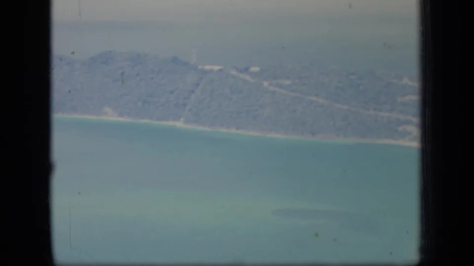 Aerial Puerto Rico coastline frame from 1970, with wooded terrain, a thin beach, turquoise water, and visible vintage film texture.