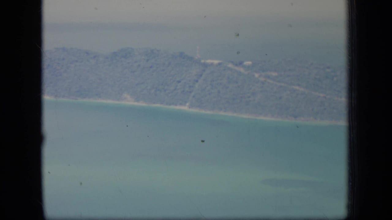 1970 Puerto Rico 8mm aerial frame showing a green coastal island edge, light beach strip, and turquoise water with dark film borders visible.