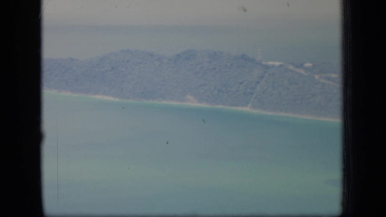 Aerial coastline with green hills, turquoise water, and a narrow pale beach.
