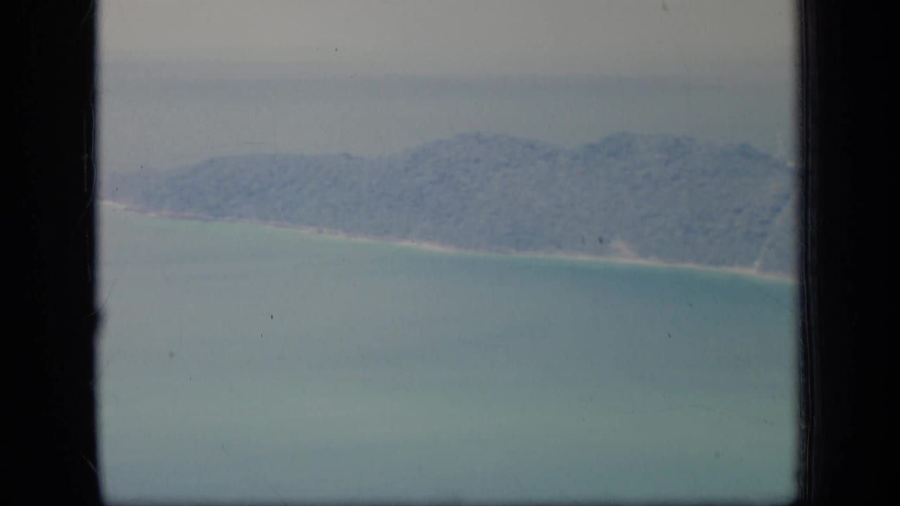 Soft aerial view of a wooded island shoreline and shallow turquoise water.