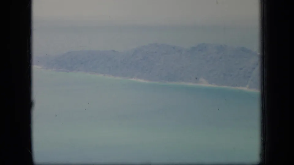 1970 Puerto Rico 8mm frame showing a softly focused aerial view of wooded coastline, pale sand, and shallow turquoise water within visible film borders.