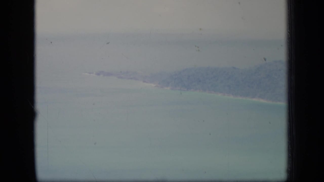 Hazy aerial view of turquoise water and a distant tree-covered coastline through dark window edges.