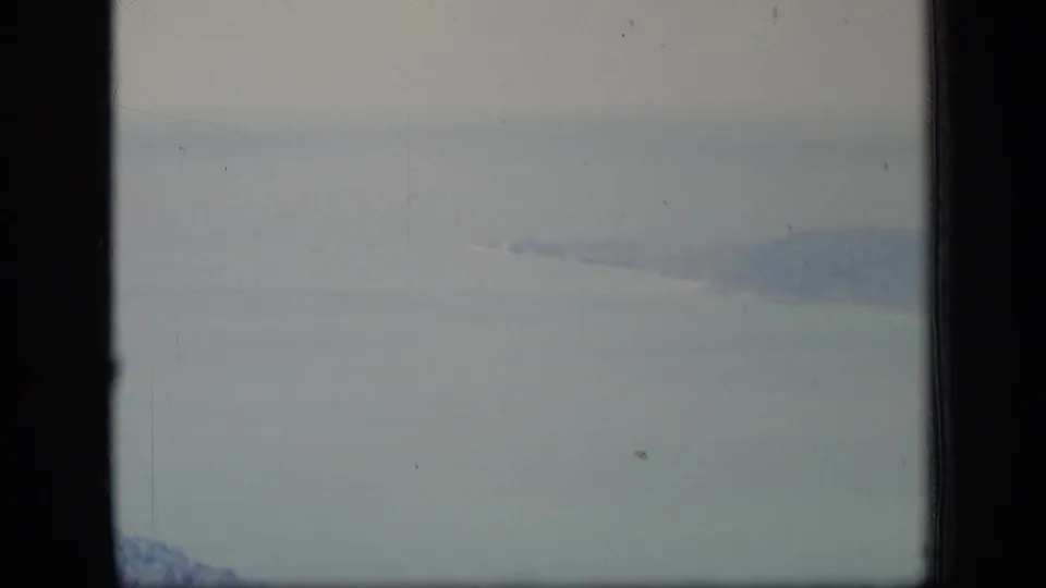 1970 Puerto Rico home-movie frame with ocean, a faint wooded shoreline, haze, and visible 8mm gate borders.