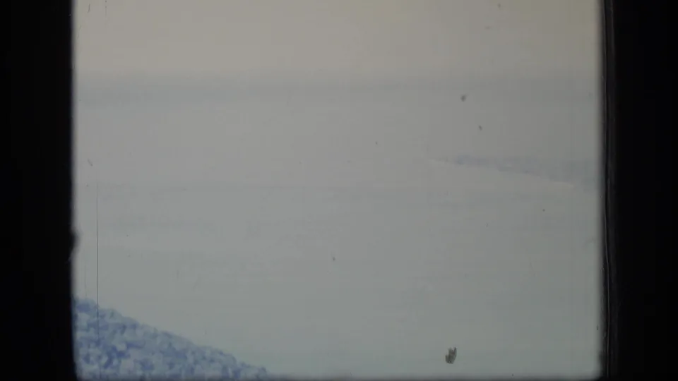1970 Puerto Rico 8mm frame showing a washed, hazy aircraft-window view of water, coastline, and forested land below.