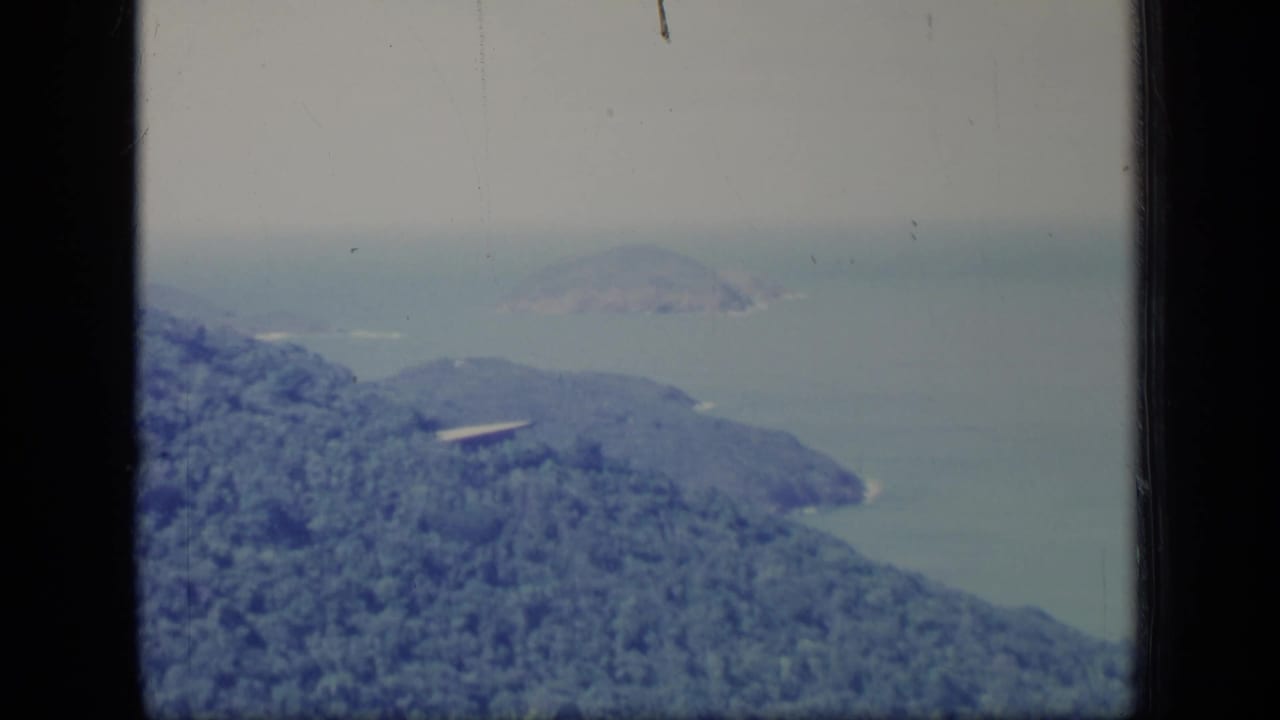 Forested hillside overlooking hazy ocean and distant islands.
