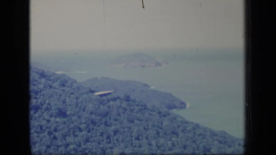 1970 Puerto Rico 8mm frame showing dense green hillside vegetation, hazy water, and distant offshore landforms.
